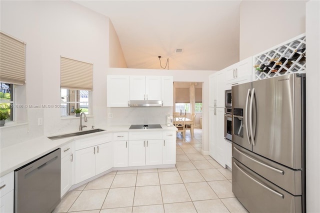 kitchen featuring light tile patterned floors, under cabinet range hood, stainless steel appliances, a sink, and white cabinetry