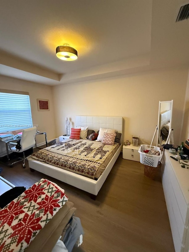 bedroom with a raised ceiling, visible vents, and wood finished floors