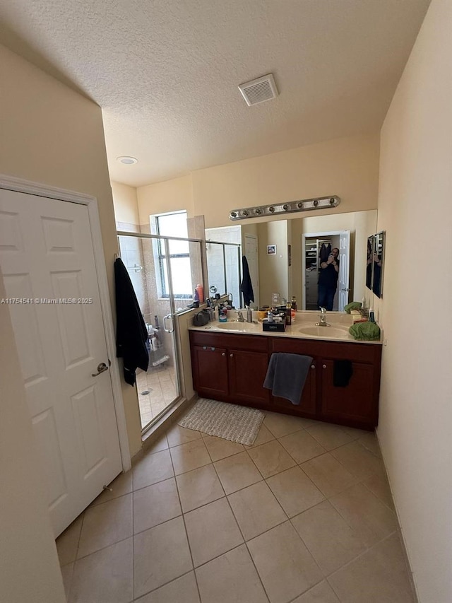 full bath with double vanity, a stall shower, a sink, a textured ceiling, and tile patterned flooring