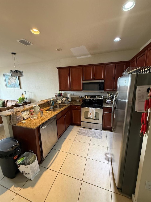 kitchen featuring light tile patterned floors, appliances with stainless steel finishes, a peninsula, stone counters, and a sink