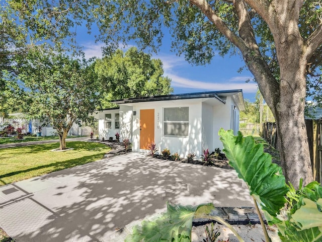 view of front of house featuring fence, a front lawn, and stucco siding