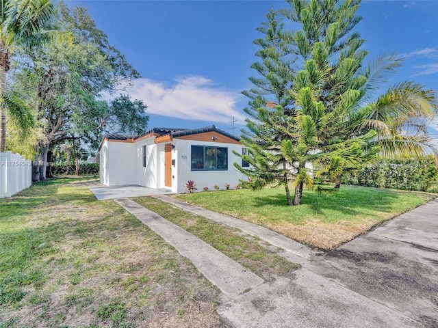 view of front of property featuring a tile roof, fence, a front lawn, and stucco siding