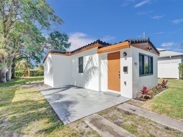 view of front of property featuring a patio, stucco siding, a front yard, fence, and a tiled roof