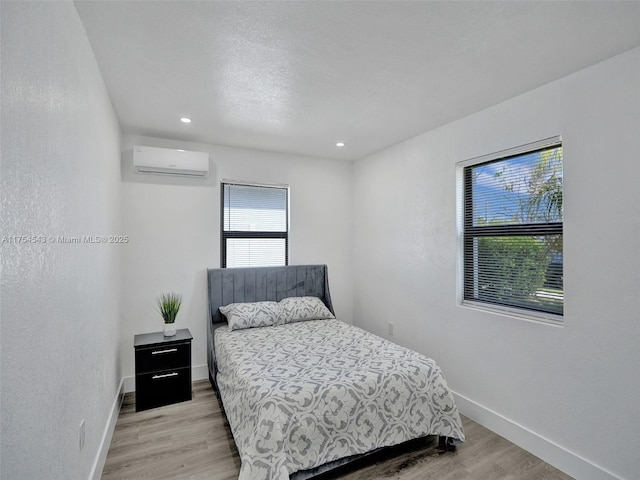 bedroom with light wood-style flooring, baseboards, and a wall mounted air conditioner