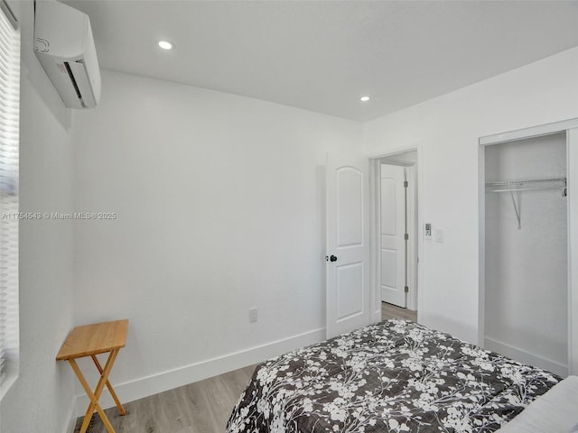 bedroom featuring recessed lighting, wood finished floors, baseboards, a wall mounted AC, and a closet