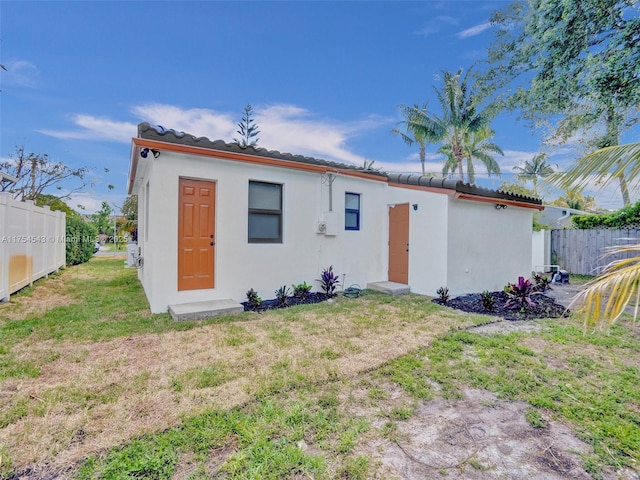 rear view of property with stucco siding, a lawn, a tiled roof, and fence