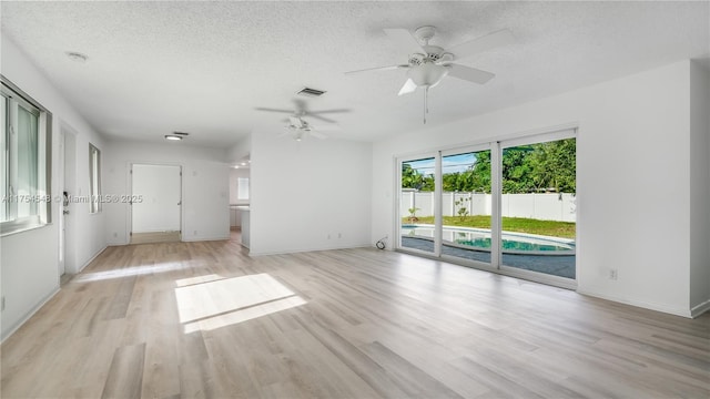 empty room with light wood-style floors, baseboards, visible vents, and a textured ceiling