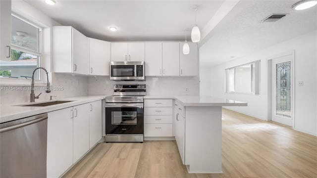 kitchen featuring a peninsula, appliances with stainless steel finishes, light countertops, and a sink