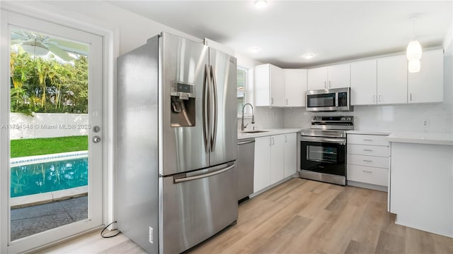 kitchen with light wood finished floors, stainless steel appliances, light countertops, white cabinets, and a sink