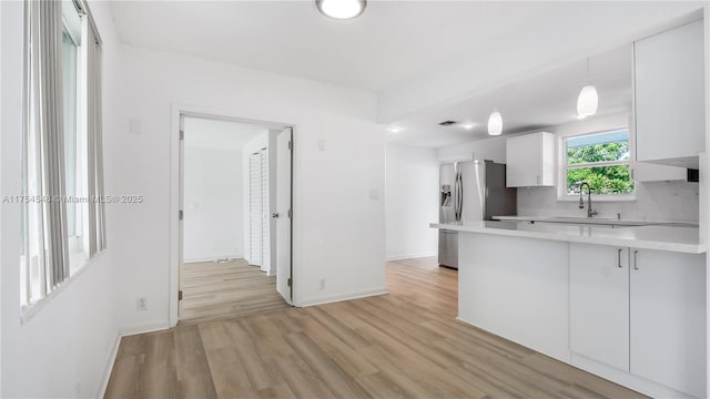 kitchen with light countertops, white cabinetry, a sink, light wood-type flooring, and a peninsula