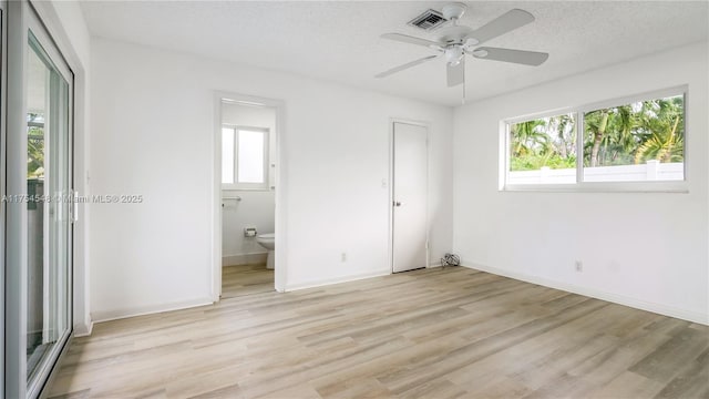 unfurnished bedroom with light wood-style floors, multiple windows, a textured ceiling, and baseboards