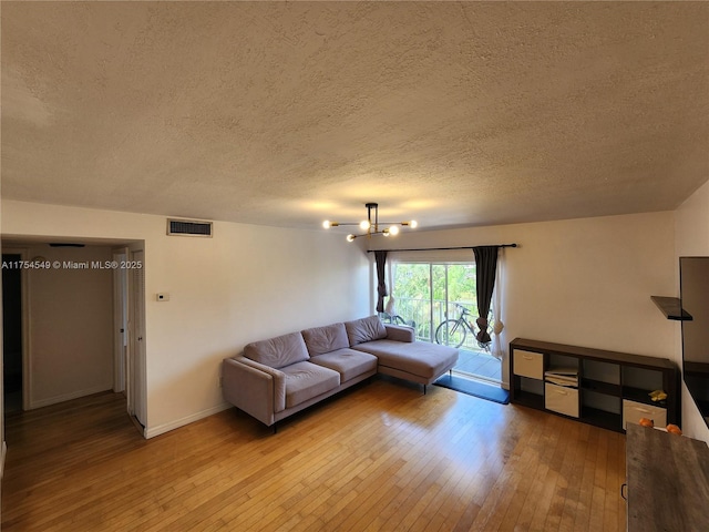 living area featuring a chandelier, a textured ceiling, light wood-style flooring, visible vents, and baseboards