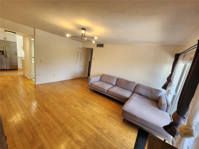 unfurnished living room featuring light wood-style floors, visible vents, a textured ceiling, and an inviting chandelier