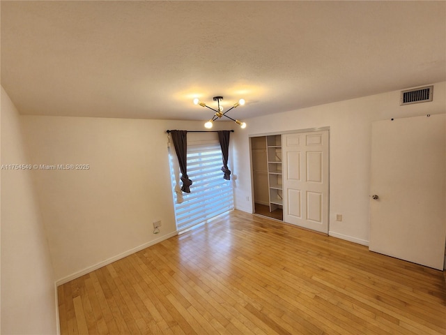 empty room featuring light wood finished floors, visible vents, and a notable chandelier