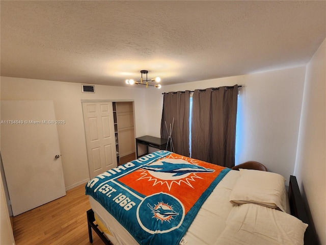 bedroom with a chandelier, light wood-type flooring, visible vents, and a textured ceiling