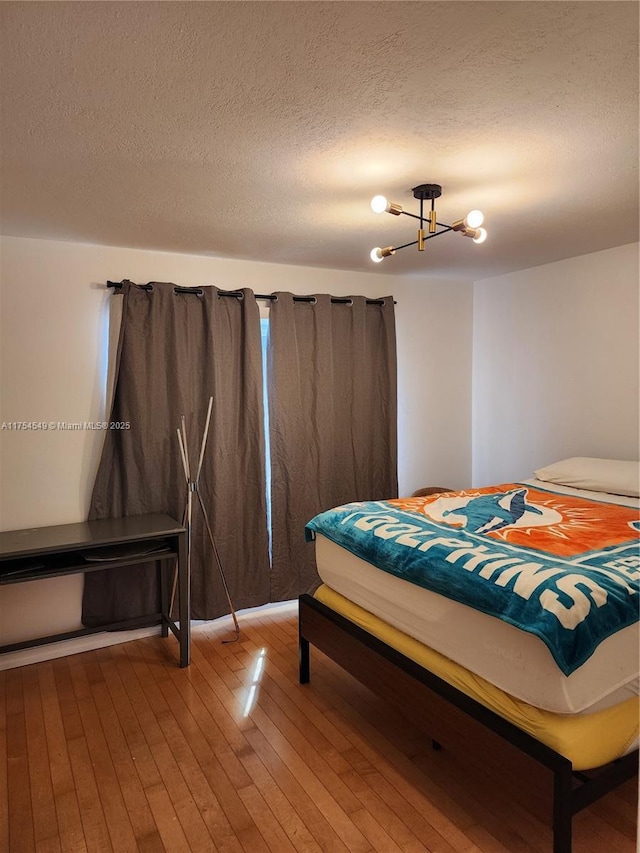 bedroom featuring a textured ceiling, light wood finished floors, and an inviting chandelier