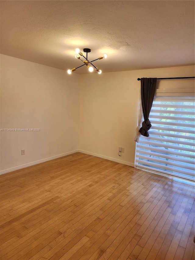 unfurnished room with a textured ceiling, baseboards, hardwood / wood-style flooring, and an inviting chandelier