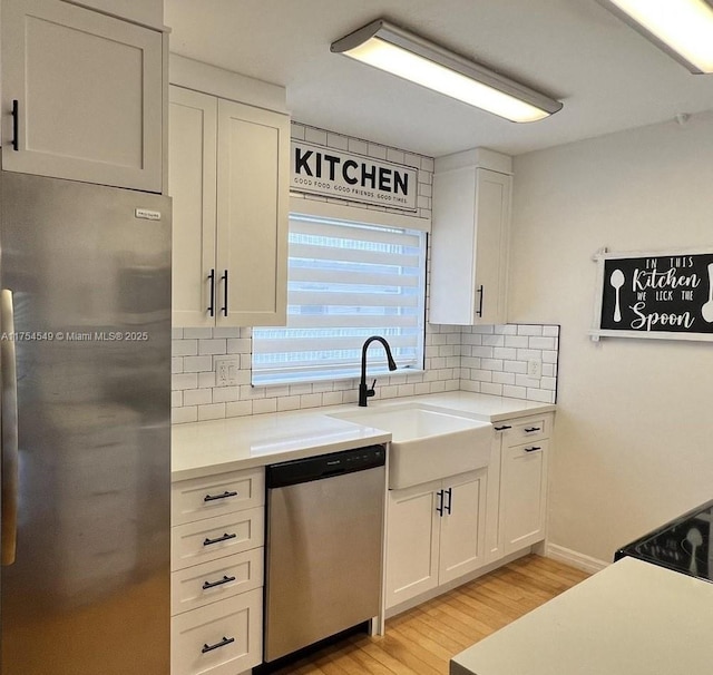 kitchen with a sink, white cabinetry, light countertops, appliances with stainless steel finishes, and backsplash