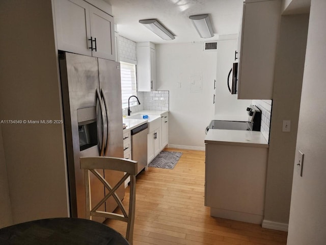 kitchen featuring visible vents, backsplash, appliances with stainless steel finishes, a sink, and light wood-type flooring