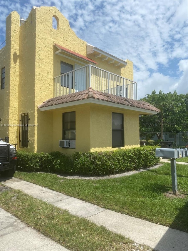 view of side of home featuring a tiled roof, a balcony, a yard, and stucco siding