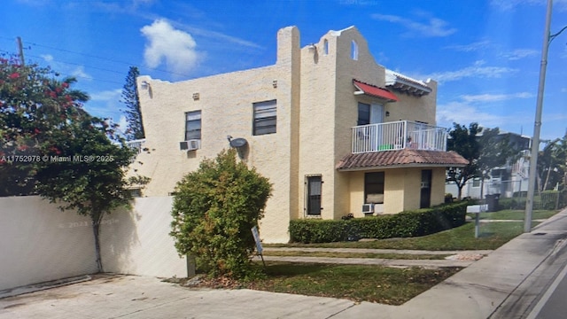 view of side of home with a balcony, a chimney, a tiled roof, cooling unit, and stucco siding