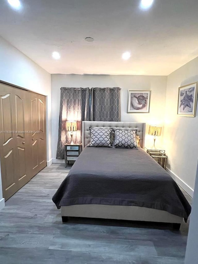 bedroom with a closet, recessed lighting, wood finished floors, and baseboards