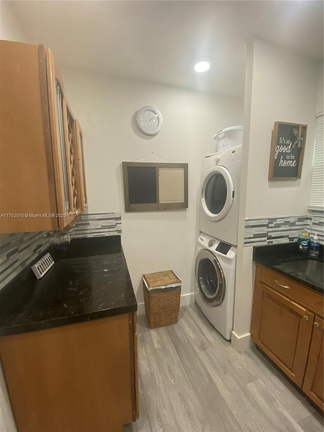 laundry room with stacked washer and dryer, a sink, light wood-type flooring, laundry area, and baseboards