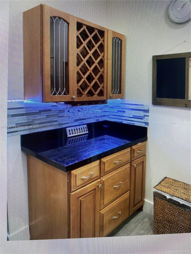 kitchen featuring dark countertops, brown cabinetry, glass insert cabinets, and decorative backsplash