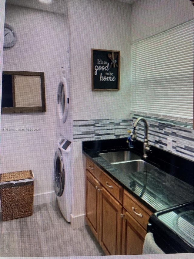 laundry area featuring laundry area, light wood-style flooring, a sink, stacked washing maching and dryer, and baseboards