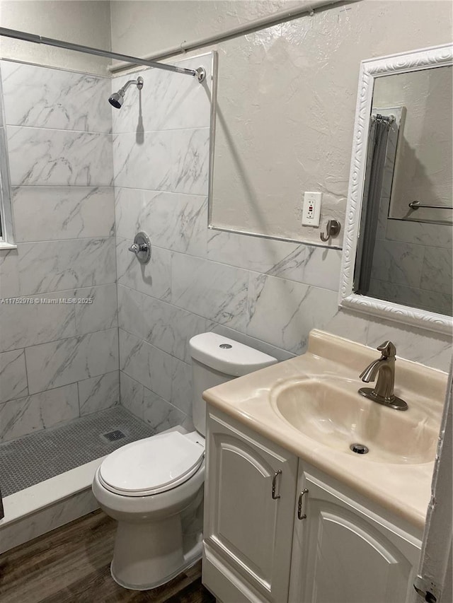 full bath with a textured wall, toilet, vanity, tile walls, and a stall shower