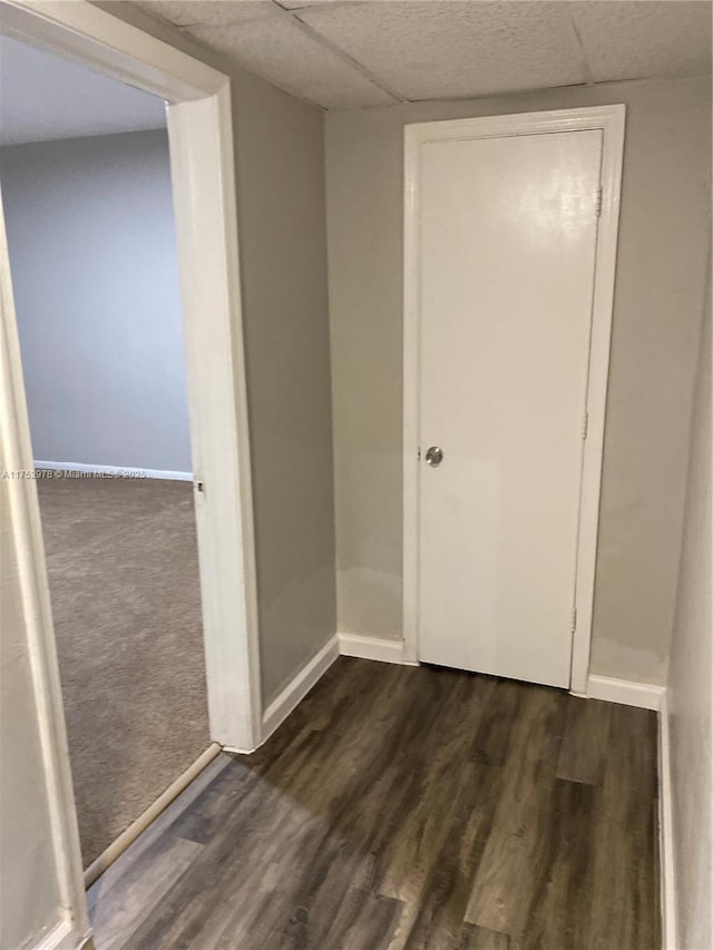 unfurnished room featuring dark wood-type flooring, a drop ceiling, and baseboards