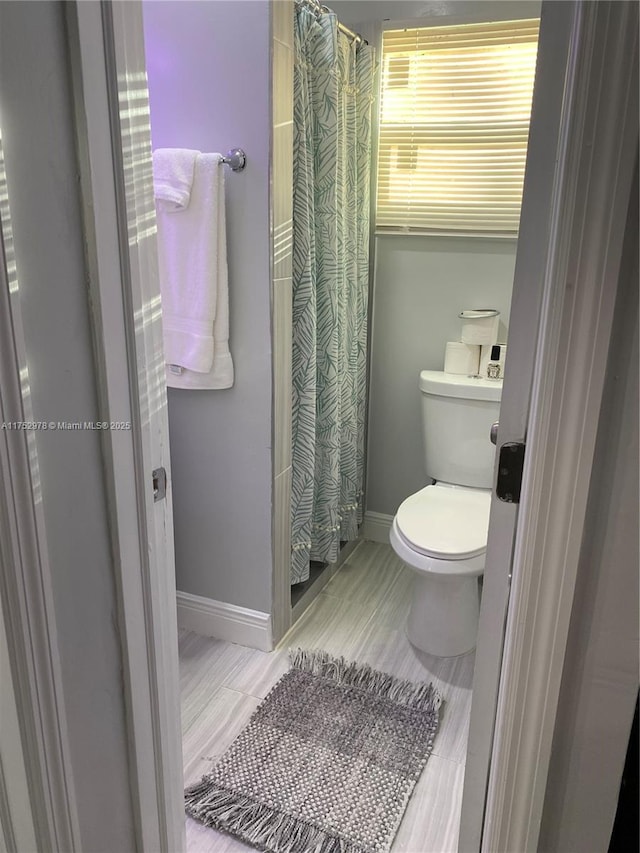 full bathroom with a shower with shower curtain, toilet, and baseboards