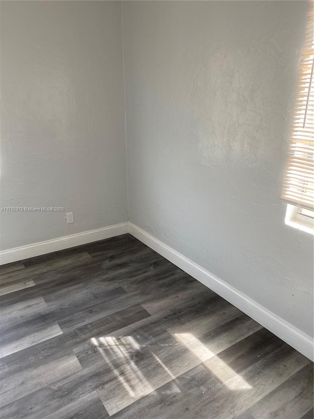 unfurnished room with dark wood-type flooring and baseboards