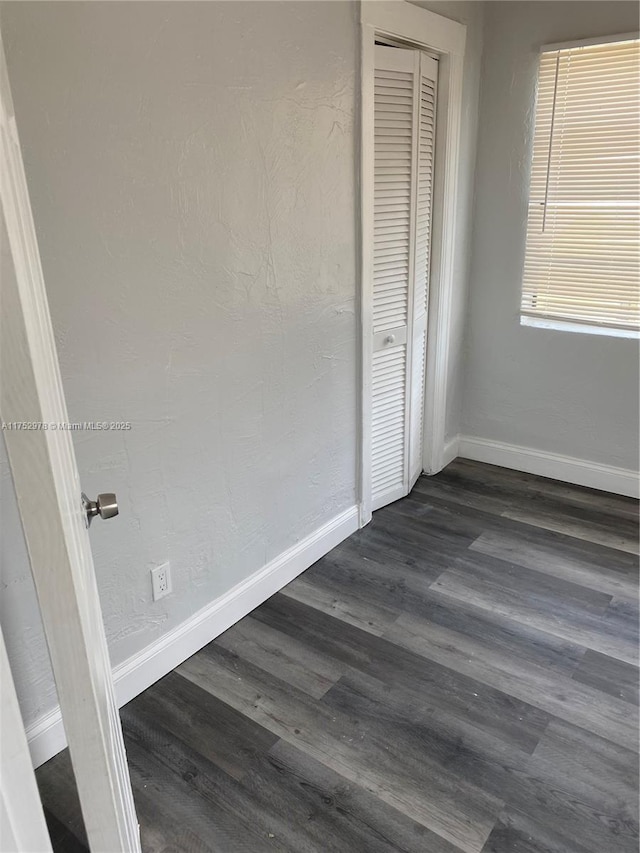 unfurnished bedroom with dark wood-style floors, baseboards, a closet, and a textured wall