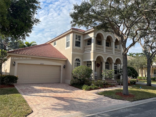 mediterranean / spanish-style home featuring decorative driveway, a tile roof, stucco siding, an attached garage, and a balcony