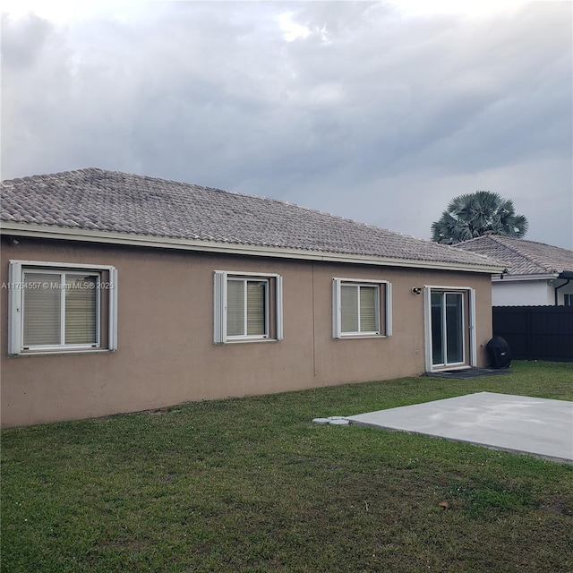 rear view of property with a patio area, a lawn, fence, and stucco siding