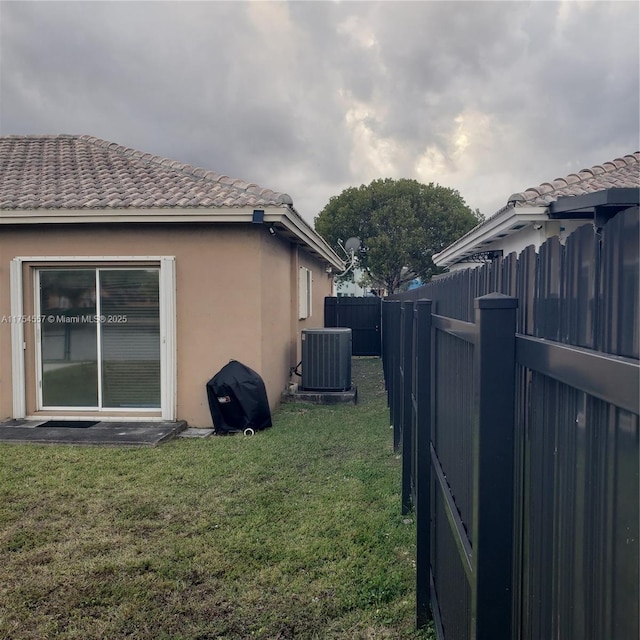 view of side of property with a tile roof, a yard, stucco siding, central AC unit, and a fenced backyard