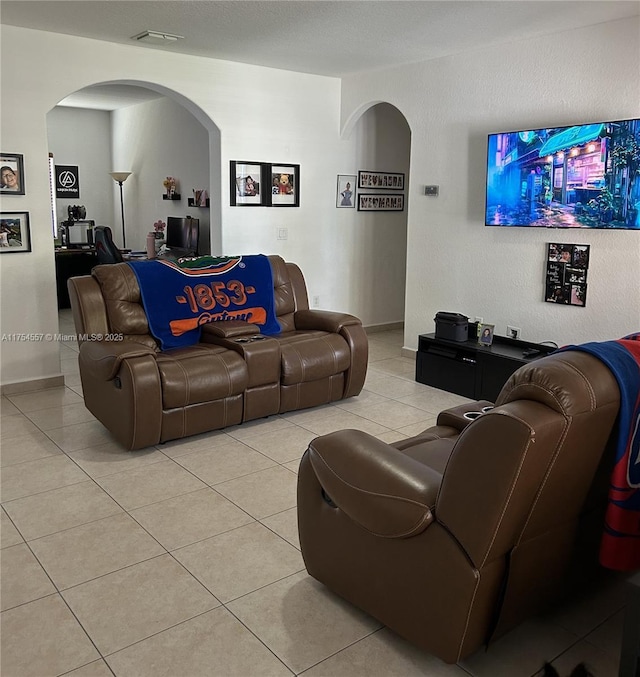 living room with arched walkways, light tile patterned floors, visible vents, and baseboards