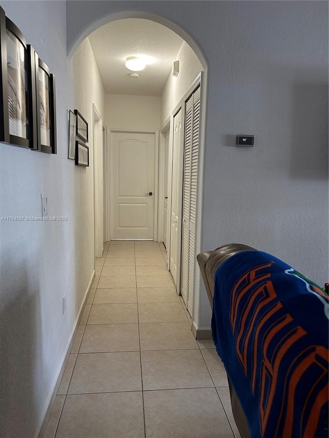 corridor featuring baseboards, arched walkways, a textured ceiling, and light tile patterned flooring