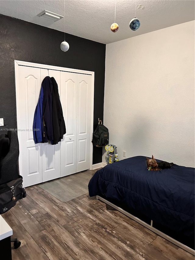 bedroom featuring a closet, visible vents, a textured wall, a textured ceiling, and wood finished floors