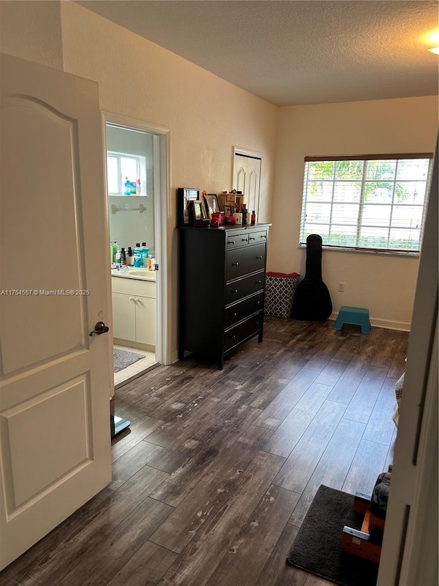 bedroom with dark wood-style flooring, a textured ceiling, and ensuite bath