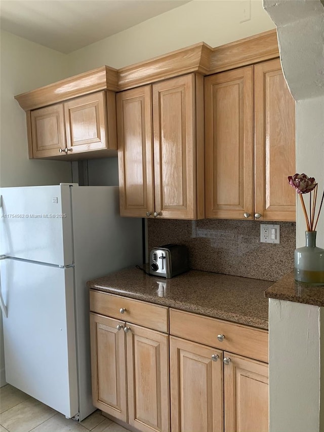 kitchen with light brown cabinetry, dark stone countertops, and freestanding refrigerator