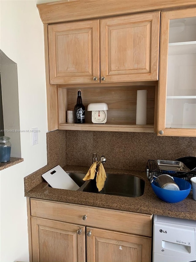 interior details featuring open shelves, dark countertops, light brown cabinetry, white dishwasher, and a sink