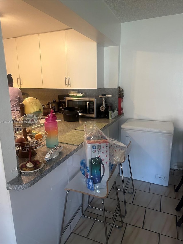 kitchen with stainless steel microwave, tile patterned flooring, white cabinets, and refrigerator