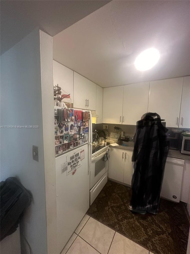 kitchen with white appliances, dark tile patterned floors, and white cabinetry