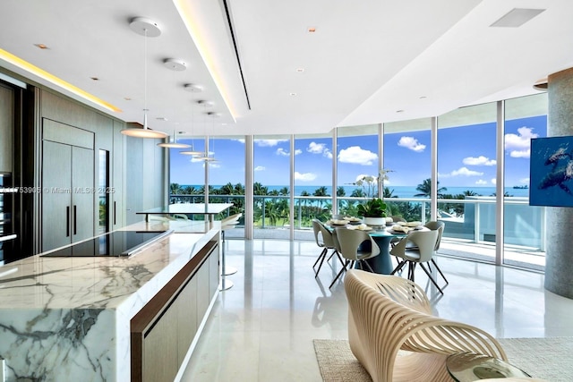 kitchen featuring modern cabinets, light stone countertops, expansive windows, black electric stovetop, and pendant lighting