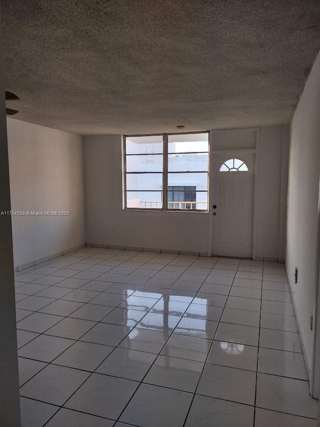 empty room with a textured ceiling, baseboards, and light tile patterned floors