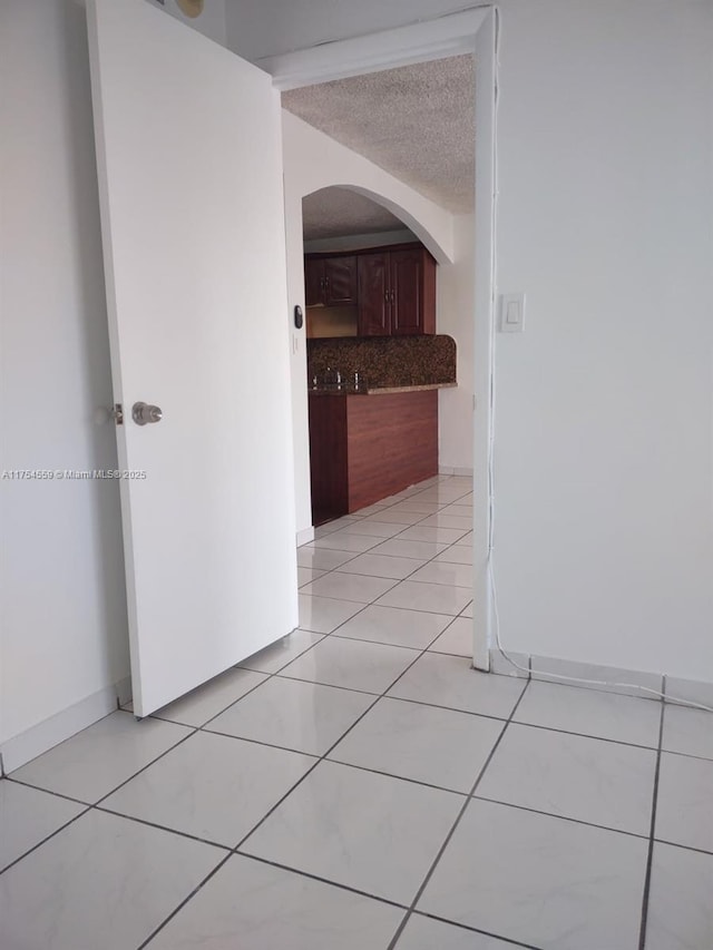 corridor featuring light tile patterned floors, a textured ceiling, arched walkways, and baseboards