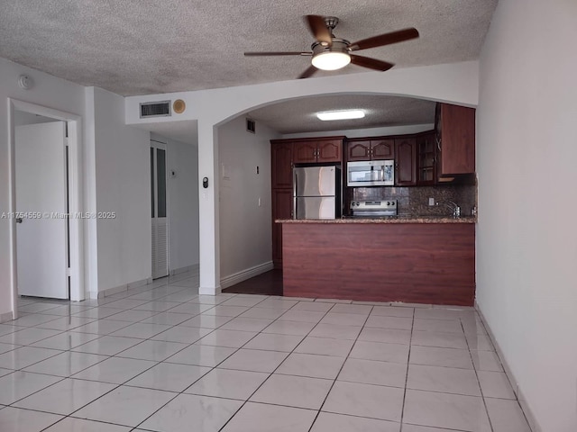 kitchen with arched walkways, light tile patterned floors, a peninsula, visible vents, and appliances with stainless steel finishes