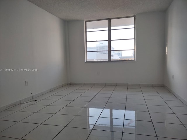 spare room featuring light tile patterned flooring, a textured ceiling, and baseboards